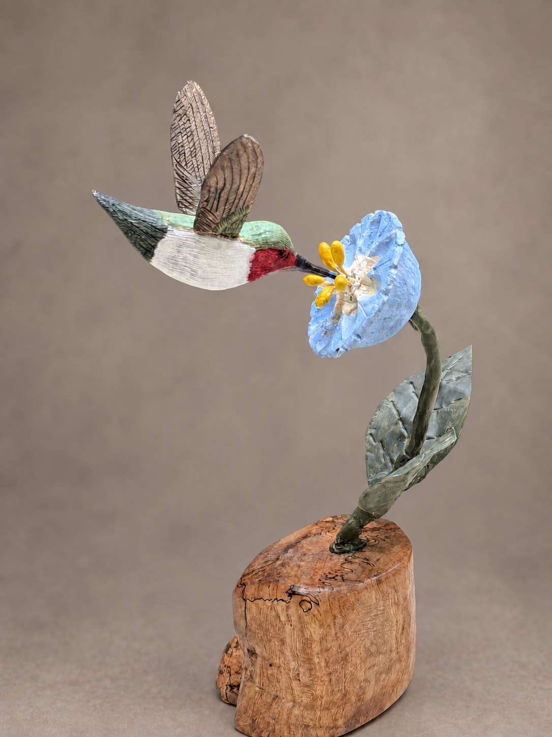Hummingbird wildlife sculpture feeding from a blue flower on a burl wood base